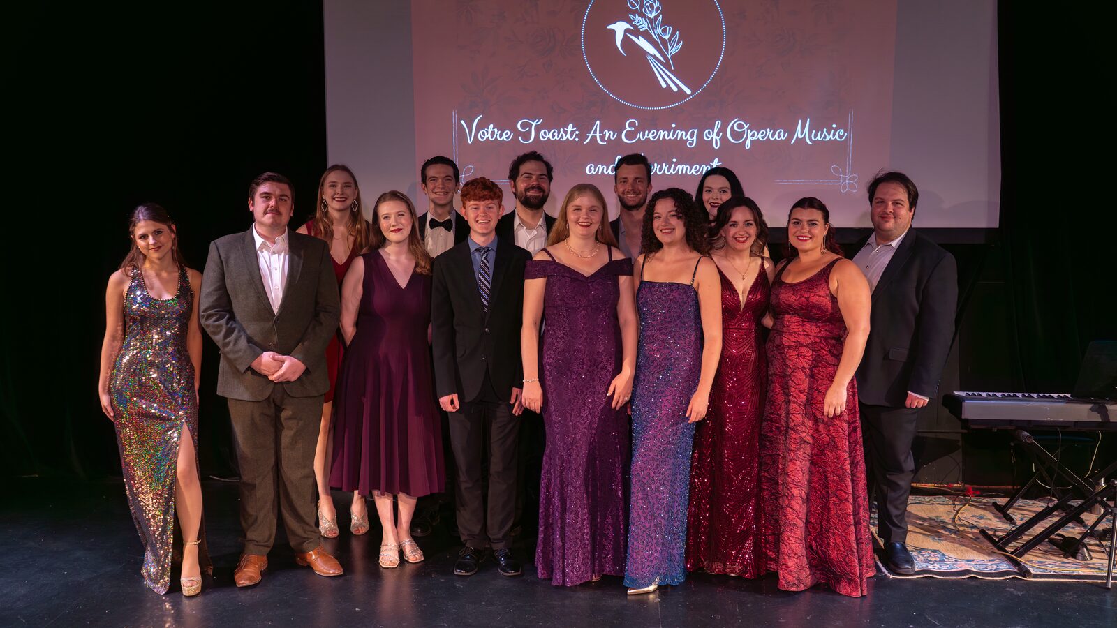 The full Magpie Opera Collective cast gathered on stage in gowns and suits, in front of the Votre Toast title screen