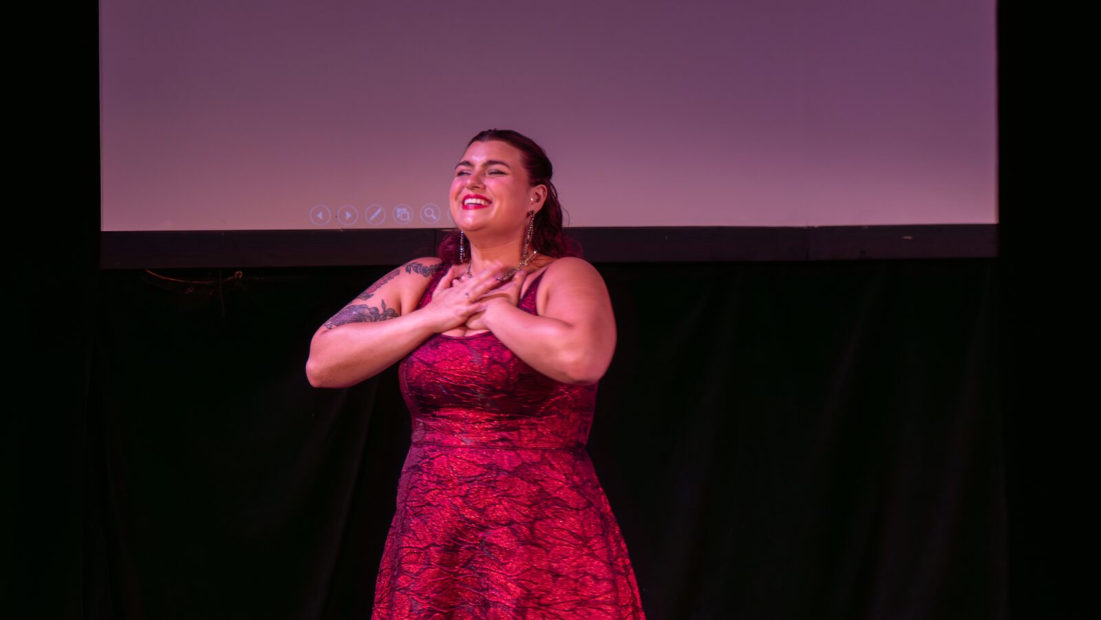 A soprano beams mid-song, hand on her heart, lit in rose-pink stage light